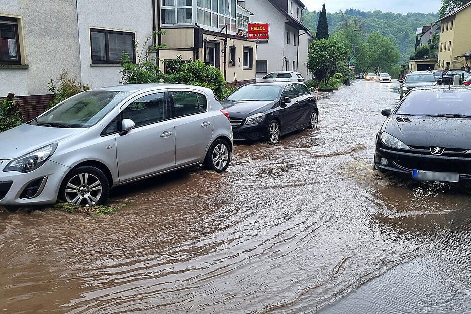 Autos fahren im Stadtteil Altenbach in Schriesheim über eine überflutete Straße.