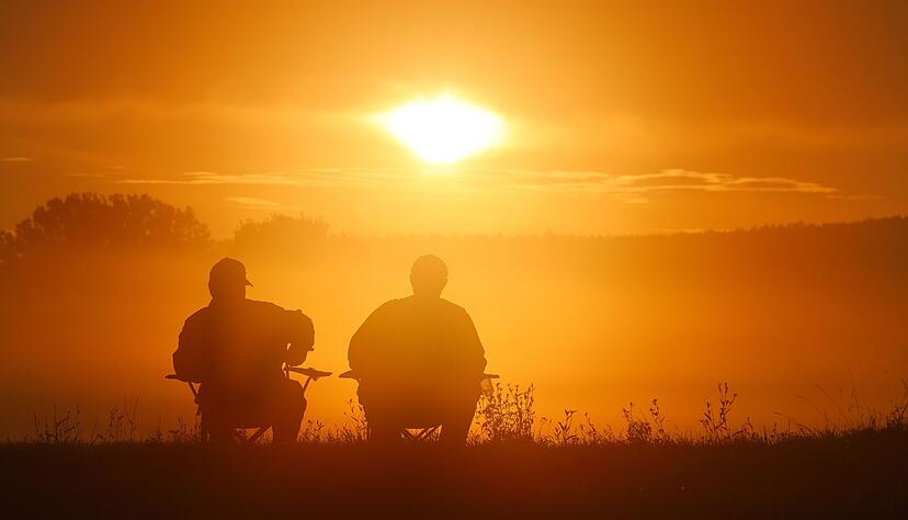 Zwei Angler sitzen auf Campingstühlen und schauen sich den Sonnenaufgang in Baden-Württemberg an. Der goldene Herbst verabschiedet sich mit einem Temperatursturz.
