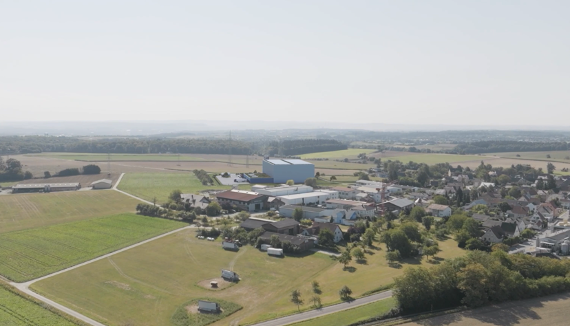 So soll sich die Logistikhalle von Mann&Schr&ouml;der in den Ort einf&uuml;gen. Das Foto zeigt eine Drohnenaufnahme, in die ein Modellentwurf der sp&auml;teren Halle (hinten im Bild) eingef&uuml;gt wurde.