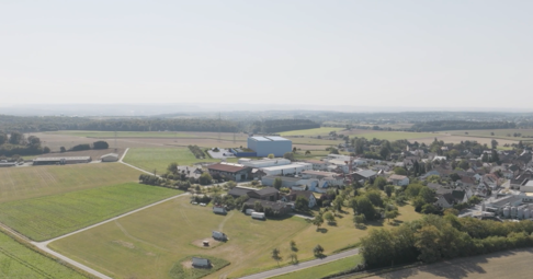 So soll sich die Logistikhalle von Mann&Schr&ouml;der in den Ort einf&uuml;gen. Das Foto zeigt eine Drohnenaufnahme, in die ein Modellentwurf der sp&auml;teren Halle (hinten im Bild) eingef&uuml;gt wurde.