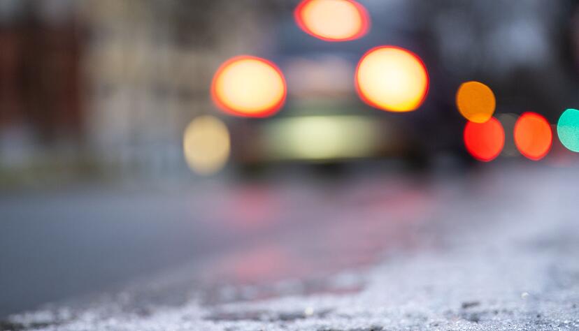Eine Eisschicht liegt auf dem Radweg, während im Hintergrund Autos über eine vereiste Straße fahren.