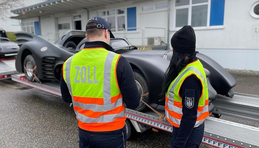 Zwei Abfertigungsbeamte stehen vor dem "Batmobil", das auf einem Anhänger angeliefert wurde. Zwei Abfertigungsbeamte stehen vor dem "Batmobil", das auf einem Anhänger angeliefert wurde.