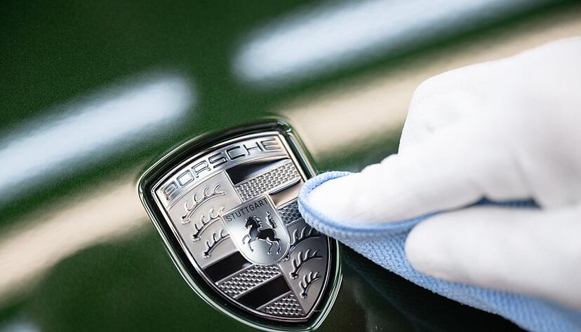 Ein Mitarbeiter der Porsche AG reinigt im Stammwerk in Zuffenhausen das Porsche-Wappen auf der Motorhaube eines vollelektrischen Porsche Taycan, nachdem er es angebracht hat. Ein Mitarbeiter der Porsche AG reinigt im Stammwerk in Zuffenhausen das Porsche-Wappen auf der Motorhaube eines vollelektrischen Porsche Taycan, nachdem er es angebracht hat.