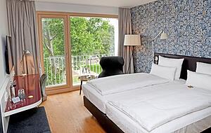 Blick in ein Standard-Doppelzimmer mit großem Bett, französischem Balkon und kleiner Sitzecke. Blick in ein Standard-Doppelzimmer mit großem Bett, französischem Balkon und kleiner Sitzecke.