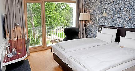 Blick in ein Standard-Doppelzimmer mit großem Bett, französischem Balkon und kleiner Sitzecke. Blick in ein Standard-Doppelzimmer mit großem Bett, französischem Balkon und kleiner Sitzecke.