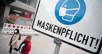 Zwei Passantinnen gehen in der Heilbronner Fußgängerzone hinter einem Schild vorbei, auf dem «Maskenpflicht» steht. Wer aus geringer Distanz angeniest oder angehustet wird, läuft trotz Mund-Nasen-Masken Gefahr, sich mit dem Coronavirus anzustecken. Foto: dpa