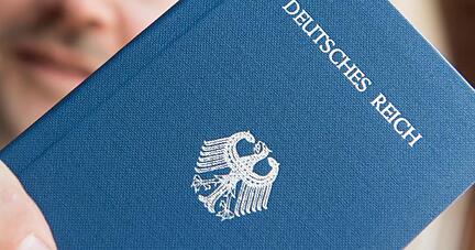 Ein Mann hält ein Heft mit dem Aufdruck «Deutsches Reich Reisepass» in der Hand.