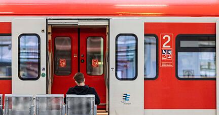 Ein Mann sitzt an einem Bahnhof vor einem Regionalzug auf der Bank.
