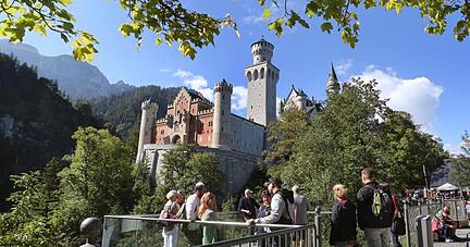 Touristen stehen an einer Aussichtsplattform unterhalb des Schlosses Neuschwanstein.
