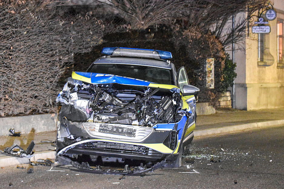Ein demoliertes Polizeiauto steht auf einer Straße. Ein Mann hat in Grünsfeld einen Bagger gestohlen, damit eine Baufirma und Streifenwagen beschädigt und drei Polizisten verletzt.