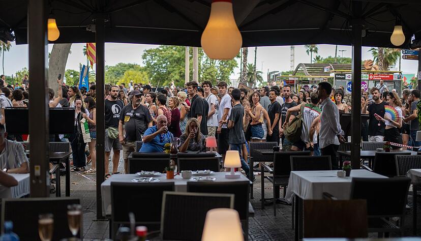 Ein Mann und eine Frau auf der Terrasse eines Restaurants in Barcelona lassen sich von vorbeiziehenden Demonstranten gegen den Massentourismus offenbar nicht aus der Ruhe bringen. Ein Mann und eine Frau auf der Terrasse eines Restaurants in Barcelona lassen sich von vorbeiziehenden Demonstranten gegen den Massentourismus offenbar nicht aus der Ruhe bringen.
