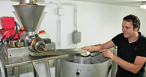 Pressvorgang in der Ölmühle: Links kommt die übrig gebliebene Leinsaat in Form von Pellets heraus, rechts fängt Stefan Kerner kaltgepresstes Leinöl auf.
Foto: Ute Plückthun
