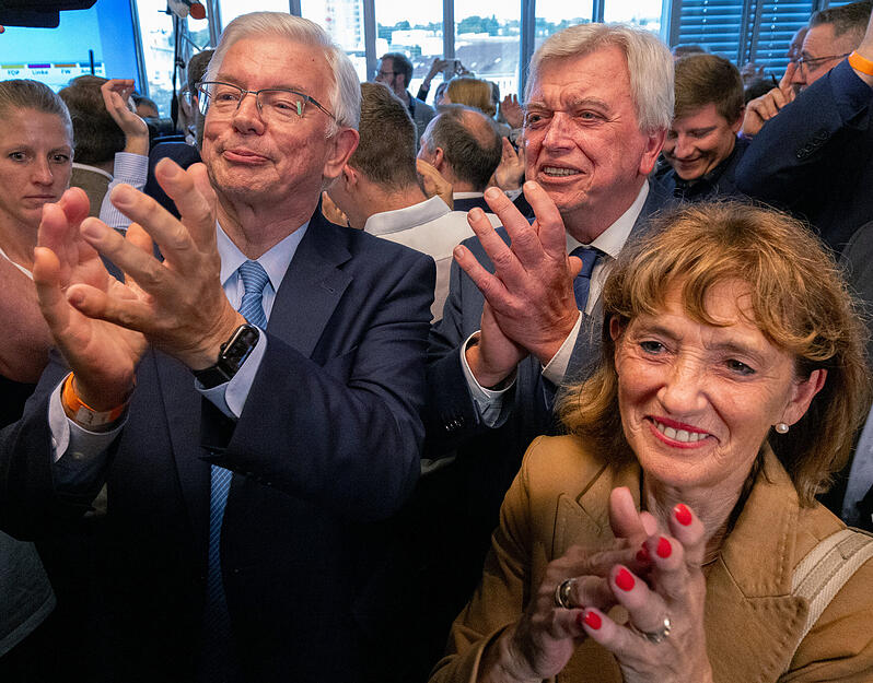 Roland Koch (CDU, l-r), ehemaliger Ministerpräsident des Landes Hessen, Volker Bouffier (CDU), ehemaliger Ministerpräsident des Landes Hessen, und seine Frau Ursula Bouffier (vorne) reagieren nach der Veröffentlichung der ersten Prognose zur Landtagswahl in Hessen.