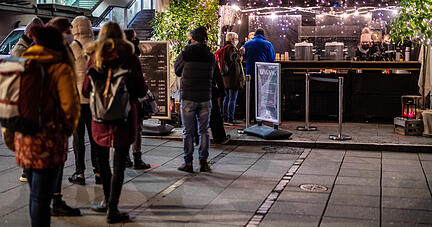 Menschen stehen während der Corona-Pandemie auf dem Schlossplatz an einem Gastronomiestand an, an dem auch Glühwein ausgeschenkt wird. Baden-Württembergs Gesundheitsminister Lucha (Grüne) will den Betrieb von Glühweinständen und anderen Schankstätten im Freien einschränken. Foto: dpa