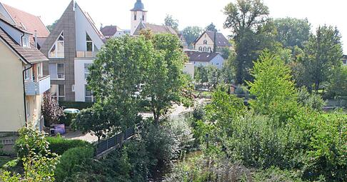 Die Kupfer &minus; ein Nebenfluss der Kocher &minus; schlängelt sich durch den Ort. Im Hintergrund erhebt sich der Turm der evangelischen Kirche. In deren Nachbarschaft stand einst auch ein sandsteinernes Schulgebäude.