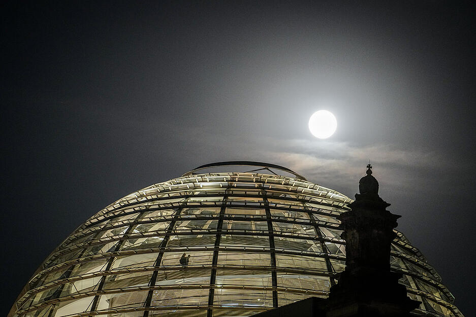 Der Vollmond leuchtet hell über der Kuppel des Reichstagsgebäudes in Berlin.