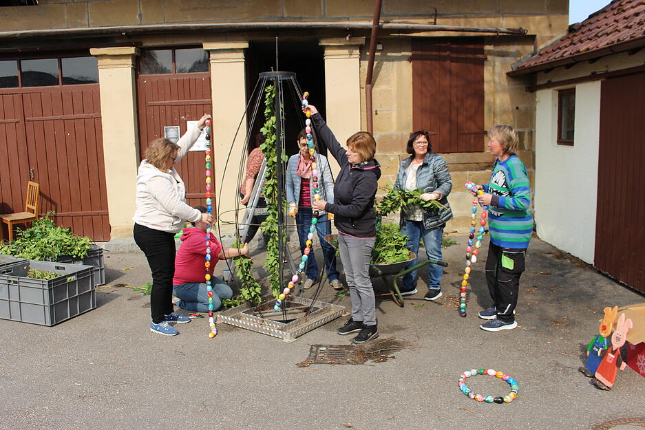Zwei Wochen vor Ostern ist vor dem Backhaus in Weinsberg-Gellmersbach Bianca Barthau vom Vorstand des Landfrauenvereins mit sieben Landfrauen damit besch&auml;ftigt, ein gro&szlig;es Osterei als Osterschmuck f&uuml;r den Dorfplatz vor der Kirche herzustellen.  Sie schneiden, b&uuml;ndeln und binden Efeuranken an das gro&szlig;e eierf&ouml;rmige Metallger&uuml;st. Sie schneiden, b&uuml;ndeln und binden Efeuranken an das gro&szlig;e eierf&ouml;rmige Metallger&uuml;st. Das schm&uuml;cken die Frauen anschlie&szlig;end mit Girlanden aus bunten Kunststoffeiern.