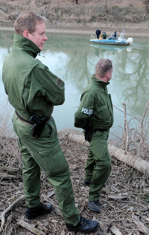 Beamte der Polizei beobachten ein Boot der Wasserschutzpolizei im Rhein bei Mannheim. Nach dem gewaltsamen Tod von drei Georgiern im Raum Ludwigshafen, die im Altrhein gefunden wurden, suchen die Beamten nun an der Fundstelle nach weiteren Spuren und der Tatwaffe.