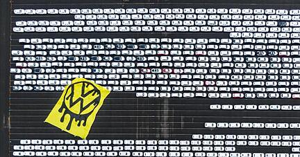 Greenpeace-Aktivisten breiten ein riesiges Protesttransparent über Autos aus, die auf dem Verladeplatz von VW im Emdener Hafen stehen.