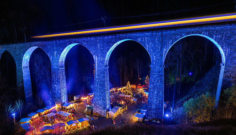 Die Höllentalbahn fährt über das beleuchtete Viadukt über der Ravennaschlucht, während darunter der Weihnachtsmarkt stattfindet.