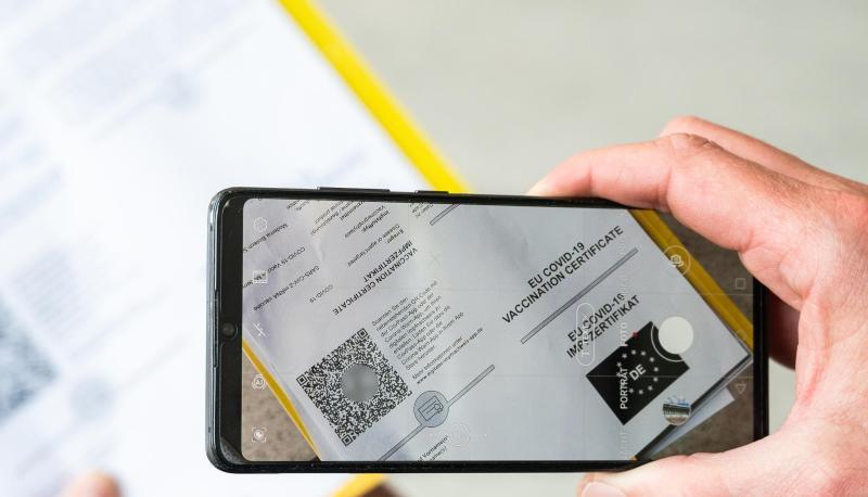 Ein Mann scannt mit einem Handy ein Dokument für den Digitalen Impfnachweis.