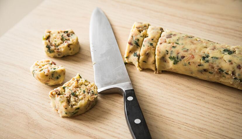 F&uuml;r die Zubereitung der Kartoffelpl&auml;tzchen wird zun&auml;chst eine Teigrolle aus fertigem Kartoffelteig (&laquo;halb und halb&raquo;), R&ouml;stzwiebeln, Petersilie, Bacon, Pfeffer, Salz und Muskatbl&uuml;te geformt und dann in Scheiben geschnitten.