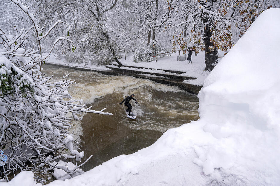 Ein Mann surft bei eisigen Temperaturen mit seinem Surfbrett auf dem Eisbach im Englischen Garten.
