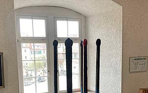 Wie Zündhölzer stehen die blau-gelben Stelen im Fenster. Eines ist oben rot.
