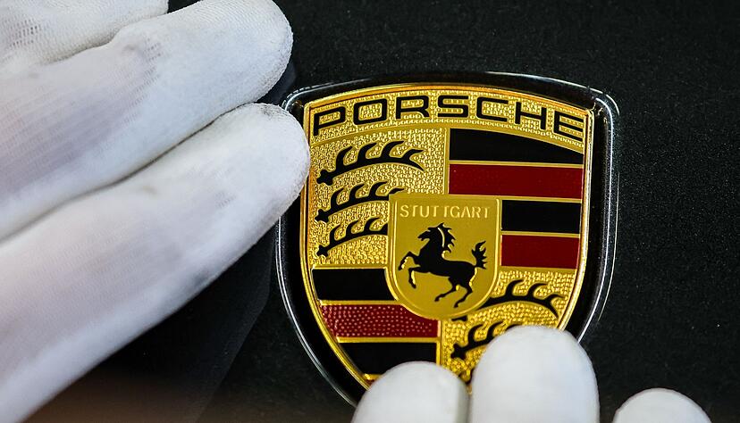 Ein Mitarbeiter befestigt das Markenlogo an einem Porsche im Werk Leipzig.