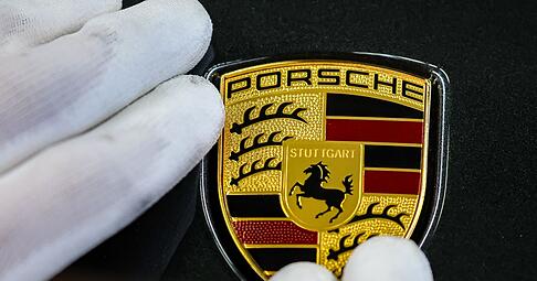 Ein Mitarbeiter befestigt das Markenlogo an einem Porsche im Werk Leipzig.