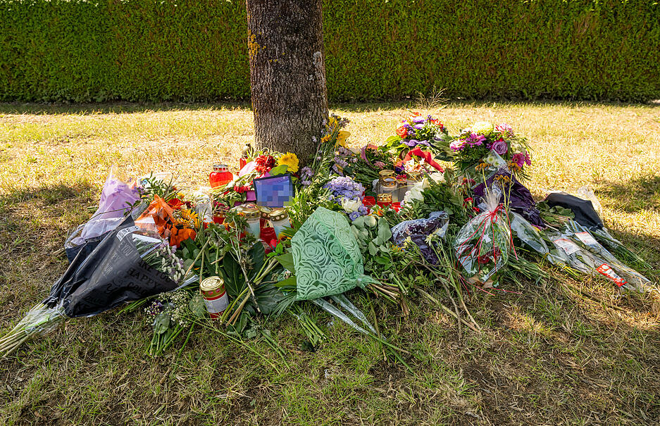 Blumen, Kerzen und Bilder liegen an einem Baum in der Nähe von Ingolstadt. In der Nähe war am 17. August 2022 eine weibliche Leiche in einem Pkw entdeckt worden.
