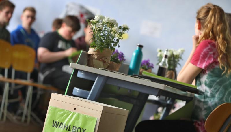 Mitglieder der Grünen Jugend Baden-Württemberg sitzen bei ihrer Landesmitgliederversammlung hinter zwei Wahlboxen.