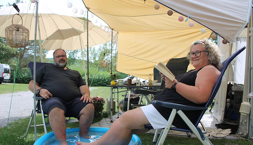 Sigrid und Dirk Buhren haben es sich unter Sonnenschirmen vor ihrem Wohnwagen auf dem Campingpark am Breitenauer See bequem gemacht. Gegen die große Hitze hilft es, die Füße im Kinderplanschbecken zu kühlen.