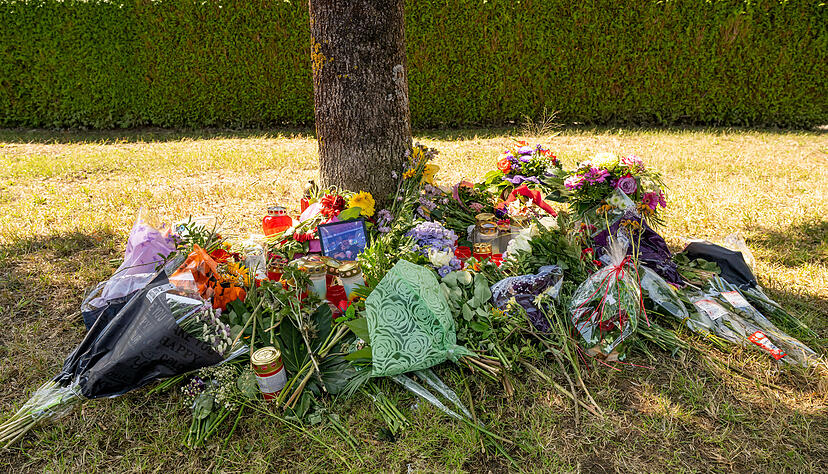 Blumen, Kerzen und Bilder liegen an einem Baum, in dessen Nähe am 17.08.2022 eine weibliche Leiche in einem Auto entdeckt wurde.