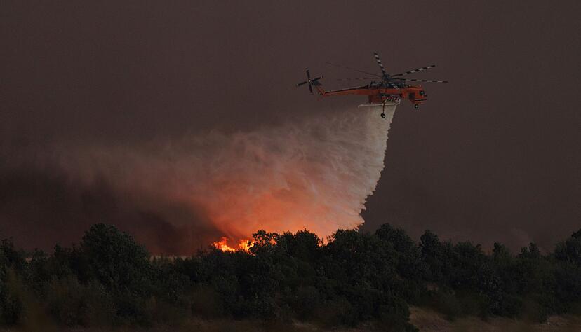 Ein Hubschrauber wirft Wasser über dem Dorf Avantas ab. Stürmische Winde fachen die Flammen der Waldbrände in ganz Griechenland an.