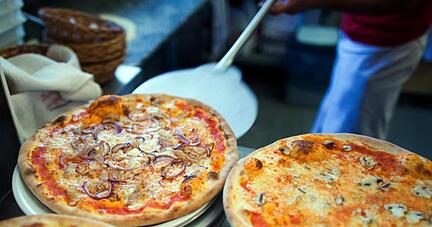 In einer Pizzeria liegen fertige Pizzen auf Tellern. Foto: Arno Burgi/Archiv