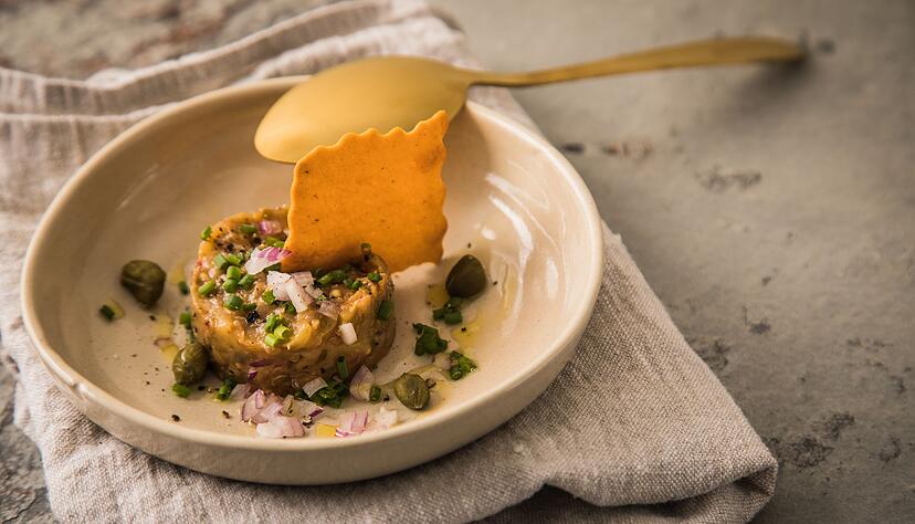In den Niederlanden gibt es Filet Americain in verschiedenen Versionen, zur Abwechslung oder f&uuml;r Vegetarier als Taler aus Auberginen-Tatar mit Kapern, Schnittlauch, Oliven&ouml;l und einem Cracker.