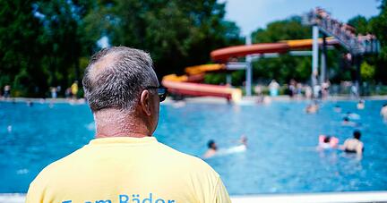 Ein Bademeister steht im Herzogenriedbad vor einem Schwimmbecken mit Wasserrutsche.