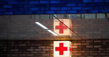 Ein Leuchtkasten mit einem roten Kreuz hängt vor der Notaufnahme eines Krankenhauses.