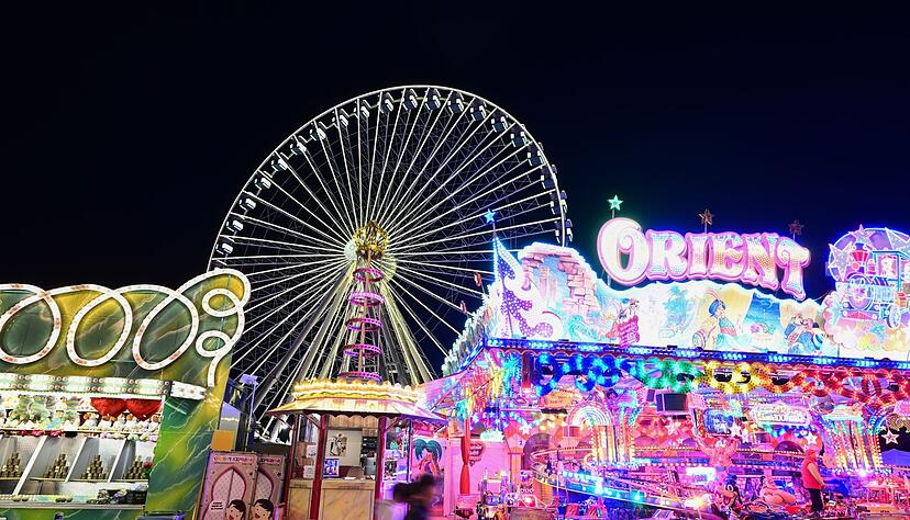 Fahrgeschäfte auf dem Volksfest Cannstatter Wasen sind im Abendlicht in Bewegung.