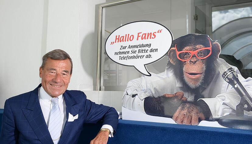 Wolfgang Grupp senior mit einem Werbeschild, auf dem der bekannte Werbe-Affe "Charly" abgebildet ist.