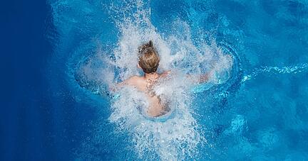Ein Junge springt in einem Schwimmbad ins Wasser.