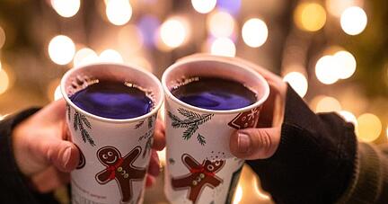 Zwei Besucherinnen eines Weihnachtsmarktes stoßen mit Glühwein an.