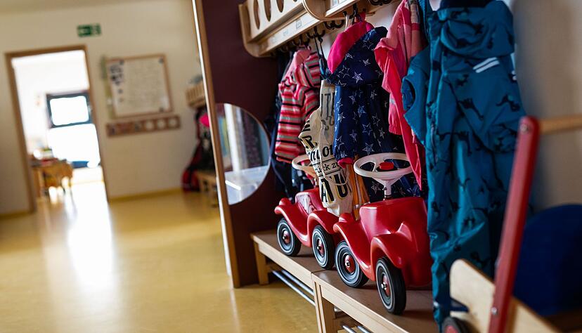 Bobbycars stehen unter Jacken von Kindern an einer Garderobe in der Kita.