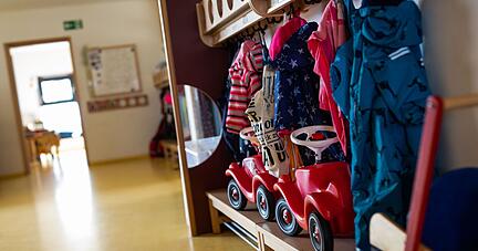 Bobbycars stehen unter Jacken von Kindern an einer Garderobe in der Kita.