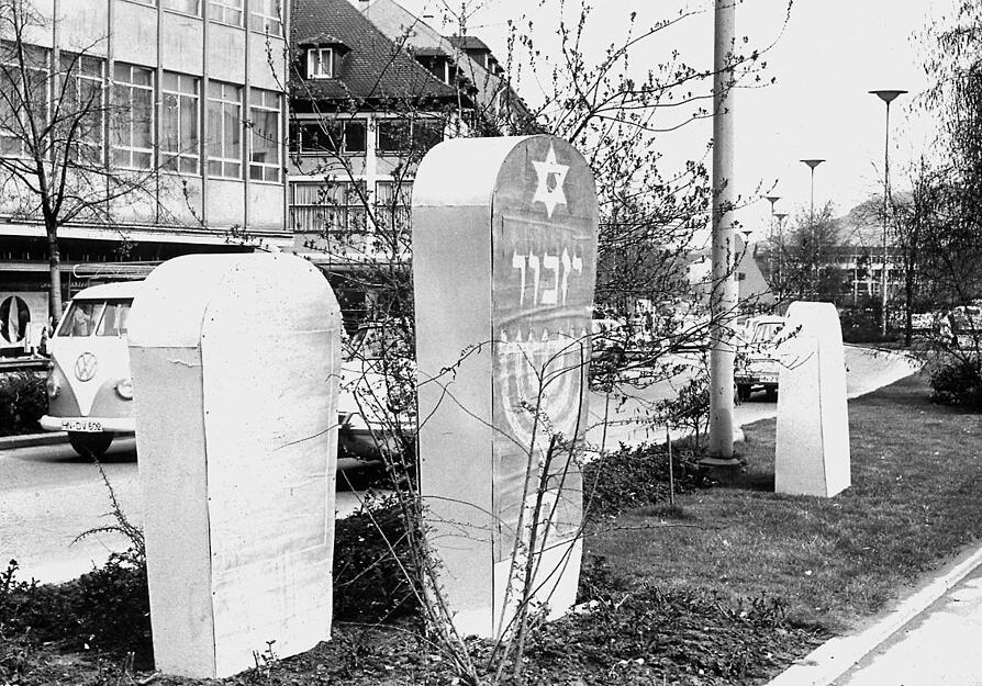 Eine Gedenktafel, ein Obelisk oder ein Gedenkstein für die in der Progromnacht 1938 abgebrannte Synagoge? 1965 stellt die Stadt Attrappen auf dem Mittelstreifen der Allee auf, um endlich zu einer Entscheidung zu kommen.