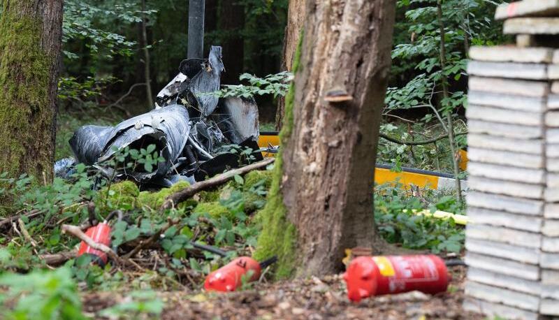 Trümmerteile eines Hubschraubers vom Typ Robinson R44 liegen in einem Wald. Trümmerteile eines Hubschraubers vom Typ Robinson R44 liegen in einem Wald.