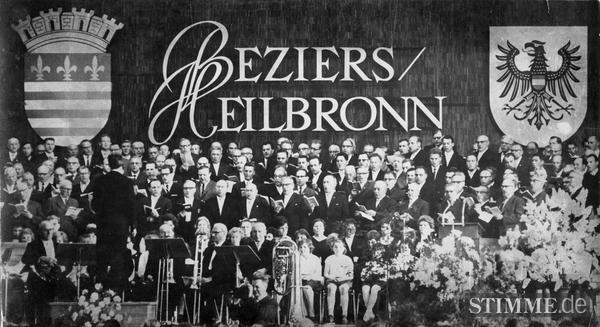 Am 20.Mai 1965 wird die Partnerschaft Heilbronn - Béziers endgültig besiegelt.
Vor den Wappen der beiden Partnerstädte stellen sich Heilbronner Sängerinnen und Sänger auf der Harmoniebühne auf.