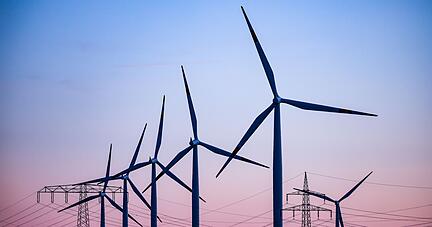 Windkraftanlagen und Hochspannungsleitungen sind vor dem Abendhimmel bei Leuna zu sehen.