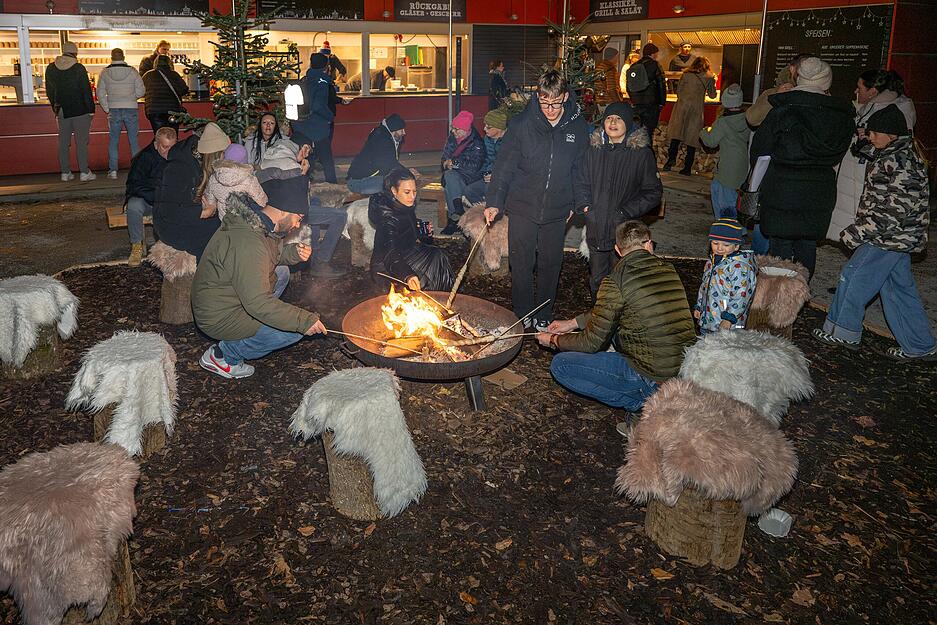 Besucher des Winterzaubers sitzen um ein Feuer herum.